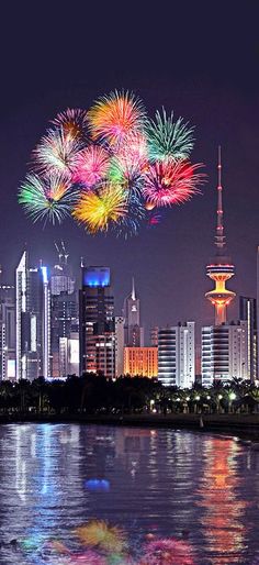 fireworks are lit up in the night sky over a cityscape and water with buildings