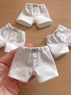 a hand is holding three white baby pants on a wooden table, and the other one has two small ones in it