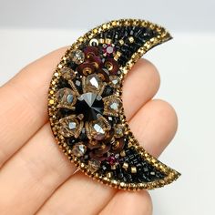 a hand holding a brooch that is shaped like the crescent moon with jewels on it