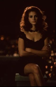 a woman sitting on top of a wooden bench in a black dress with her arms crossed