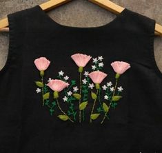 a black shirt with pink flowers embroidered on the front and white daisies in the back