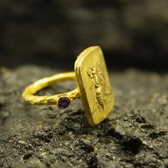 Greek Art Honey Bee  Ring | 24K Gold Plated  | Handcrafted Gold Coin Ring | Ancient Art Roman Silver Ring | Dainty Gift Our shop offer free ring sizing and color options.(Oxidized(Black),Gold Plated)Handcrafted hammered full round ring band size measures 2mm in width and 24k gold plated bronze coin 19x13 mm.Metal : 925 Sterling SilverBand Width : 2 mmGem Stone : Purple Diamond Cut Cubic ZirconiaGem Color : Green,Navy Blue,Purple,Blue,White,Red(The color you want is made for free).Gem Size : 3 mm Handmade Gold Rings As Gift For Her, Artisan Gold Ring As Gift, Artisan Gold Rings As Gift, Artisan Gold Rings Perfect As Gifts, Gold Coin Ring, Hammered Jewelry, Bee Ring, Purple Diamond, Coin Ring