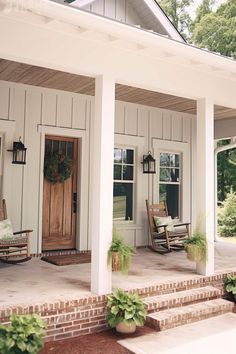 a porch with rocking chairs and potted plants on the front steps next to it