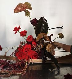 a vase filled with red flowers sitting on top of a wooden table next to a pair of scissors