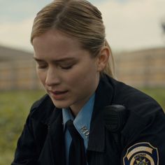 a female police officer in uniform looking down at her cell phone while sitting on the ground