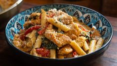 a blue bowl filled with pasta and meat covered in sauce on top of a wooden table