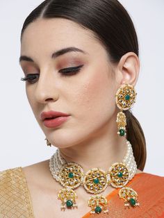 This stunning jewelry set consists of a choker necklace and a pair of matching drop earrings. The multi-stranded white pearl choker necklace shown in green and off-white color comes gold-plated with kundan stone studs & green accent beads, and secured with a drawstring closure. A pair of matching drop earrings come secured with a post and back closure. This statement piece can add impact to any outfit for any festive occasion! Product color may vary based on the monitor or screen you are using.S Festive Green Pearl Drop Jewelry, Festive Green Pearl Jewelry, Green Pearl Drop Jewelry For Festivals, White Pearl Choker, Choker Necklace Set, Pearl Choker Necklace, Stone Studs, Green Accents, Pearl Choker