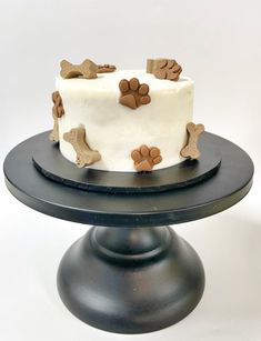 a cake with white frosting and brown dog paw decorations on the top is sitting on a black plate