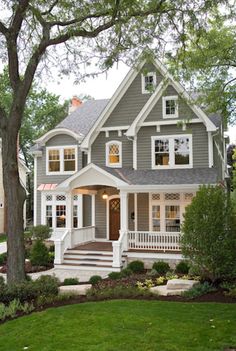 a gray house with white trim and two story windows on the second floor is surrounded by trees