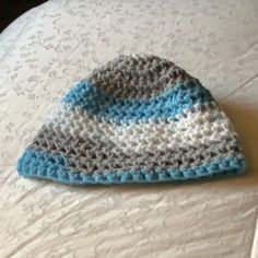 a crocheted hat sitting on top of a white bed covered in blue and gray yarn