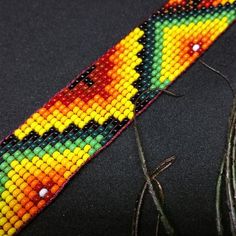 a colorful beaded bracelet sitting on top of a black table next to some thread