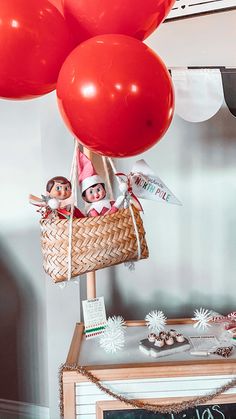 two elfs in a basket with red balloons hanging from it's side on top of a table