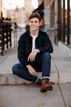 a young man is sitting on the sidewalk smiling