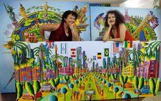 two women are posing in front of their art work that is painted on the wall