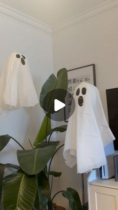 two white ghost heads hanging from the ceiling next to a plant in a living room