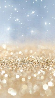 a blurry image of gold and white glitter with stars in the sky behind it