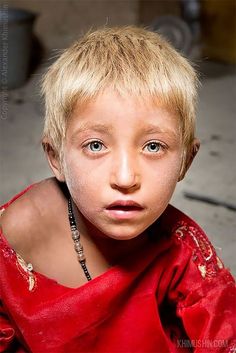 a young boy with blonde hair and blue eyes wearing a red shirt looking at the camera