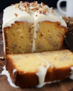 a loaf of cake with white icing and nuts on top next to a knife