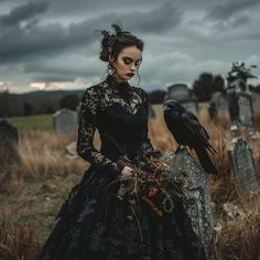 a woman in a black dress with a crow on her shoulder standing next to a grave