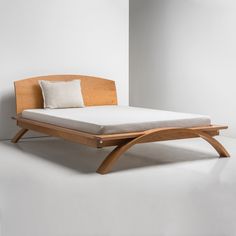 a bed with a wooden frame and mattress on top of it next to a white wall