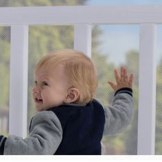 a little boy that is standing up in front of a fence with his hands out