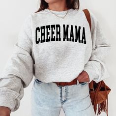 The "Cheer Mama Sweatshirt" is a sturdy and warm sweatshirt bound to keep you warm in the colder months. A pre-shrunk, classic fit sweater made with love for you & your loved ones! Sweatshirt Details: * Gildan sweatshirt - unisex fit * 50% cotton, 50% polyester * Pre-shrunk * Classic fit with no center crease * 1x1 athletic rib knit collar with spandex * Air-jet spun yarn with a soft feel and reduced pilling * Double-needle stitched collar, shoulders, armholes, cuffs, and hem * Model is wearing Casual Tops For Cheerleading In Fall, Cheerleading Fan Apparel Tops For Fall, School Spirit Sweatshirt For Cheerleading In Fall, Varsity Sweatshirt For Cheerleading In Fall, Winter Team Spirit Fleece Tops, Fall Cheerleading Top With Letter Print, Gray Fan Apparel Sweatshirt For Winter, Winter Slogan Tops For College, Team Spirit Long Sleeve Top With Lettering