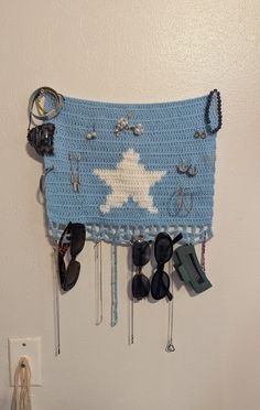 a blue and white crocheted wall hanging with sunglasses, keys, hooks and other items