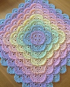 a crocheted doily on a wooden floor with a pink, blue, yellow and green design