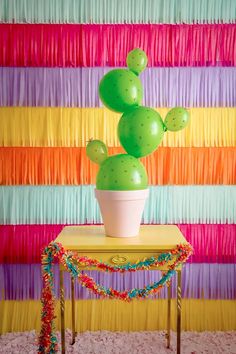 a green cactus sitting on top of a table next to a rainbow colored wallpaper