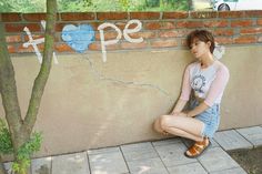 a young woman sitting on the ground next to a wall with graffiti written on it