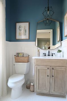 a white toilet sitting next to a sink in a bathroom under a mirror and framed pictures