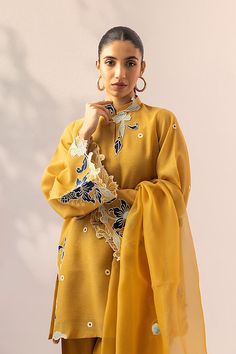 An ethereal mustard khaddi corduroy shirt elevated with applique accents adorning its neckline, sleeves and hemline. This outfit is paired with a co-ord rawsilk shalwar and an organza dupatta embellished with white pom-poms and scalloped cutwork borders. This classy yet stylish ensemble will enhance your look this fest Yellow Raw Silk Kurta With Dabka, Yellow Dabka Raw Silk Kurta, Yellow Raw Silk Kurta With Dabka Detailing, Yellow Cotton Silk Kurta With Sheer Dupatta, Yellow Long-sleeved Raw Silk Salwar Kameez, Yellow Long-sleeved Kurta With Sheer Dupatta, Yellow Long Sleeve Raw Silk Kurta, Yellow Long Sleeve Kurta With Sheer Dupatta, Yellow Cotton Silk Salwar Kameez With Long Sleeves