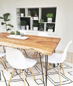 a wooden table surrounded by white chairs and potted plants