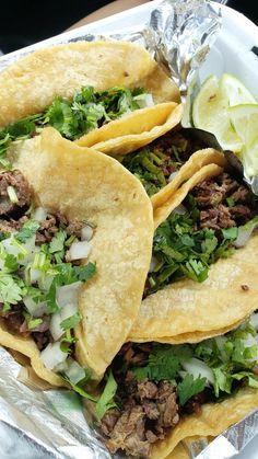 three tacos with meat, lettuce and cilantro on tin foil