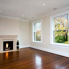 an empty room with two windows and a fireplace in the center, surrounded by wood flooring