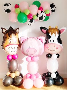 three farm animals are standing next to each other with balloons in the shape of cows