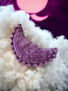 a purple brooch sitting on top of a pile of white fluffy material next to a pink moon