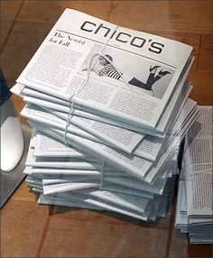 a stack of newspapers sitting on top of a wooden table next to a computer mouse