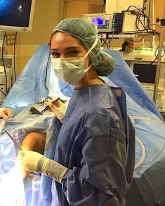 a woman in scrubs and surgical gloves standing next to a monitor screen with medical equipment on it