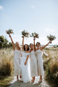 four bridesmaids in white dresses holding bouquets and posing for the camera with their arms up