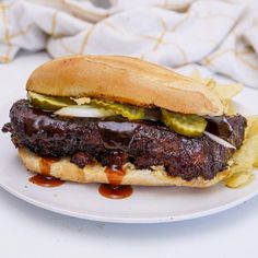 a grilled steak sandwich with pickles and onions on a plate next to chips