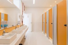 a long row of sinks in a bathroom with yellow and white doors on the walls