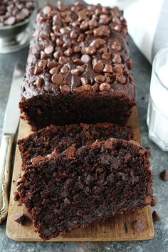 a loaf of chocolate cake sitting on top of a wooden cutting board next to a glass of milk