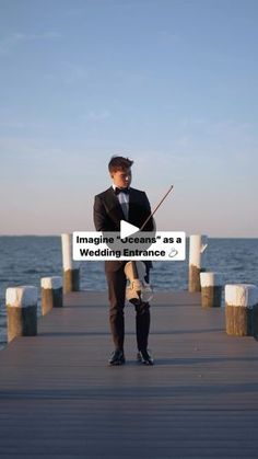 a man in a suit and tie holding a fishing pole on a pier near the ocean