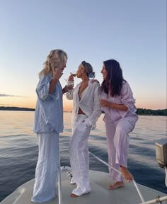 three women standing on the back of a boat talking to each other while drinking wine