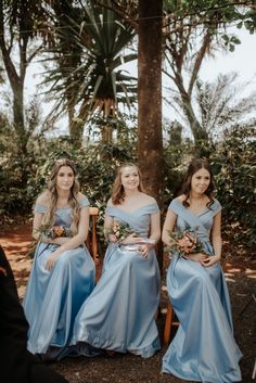 three bridesmaids in blue dresses sitting next to each other on a bench under a tree