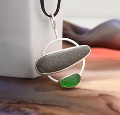 "Beachcomber's  Necklace Stone and glass combine to create this casual modern necklace. The stones I used are both from beaches in Northern England.  The elongated beach stone pairs perfectly with the translucent green sea glass pebble. Both stones are set in fine silver with solid silver backs.  The stone settings connect to a thick sterling wire frame.  A chocolate brown  1/8\" wide deerskin leather cord completes this composition. The pendant measures about 2-1/4\" tall (bottom of pendant to Sea Glass Crafts Jewellery, Beach Stones Jewelry, Silversmithing Jewelry, Pebble Jewelry, Metal Jewelry Making, Pebble Pendant, Modern Necklace, Metalsmithing Jewelry, Northern England