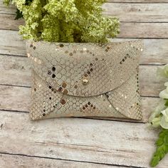 a gold sequin clutch bag sitting on top of a wooden table next to flowers