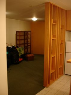 an empty room with wooden shelves and tile flooring in front of a refrigerator freezer