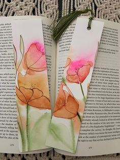 two bookmarks with watercolor flowers on them sitting on top of an open book